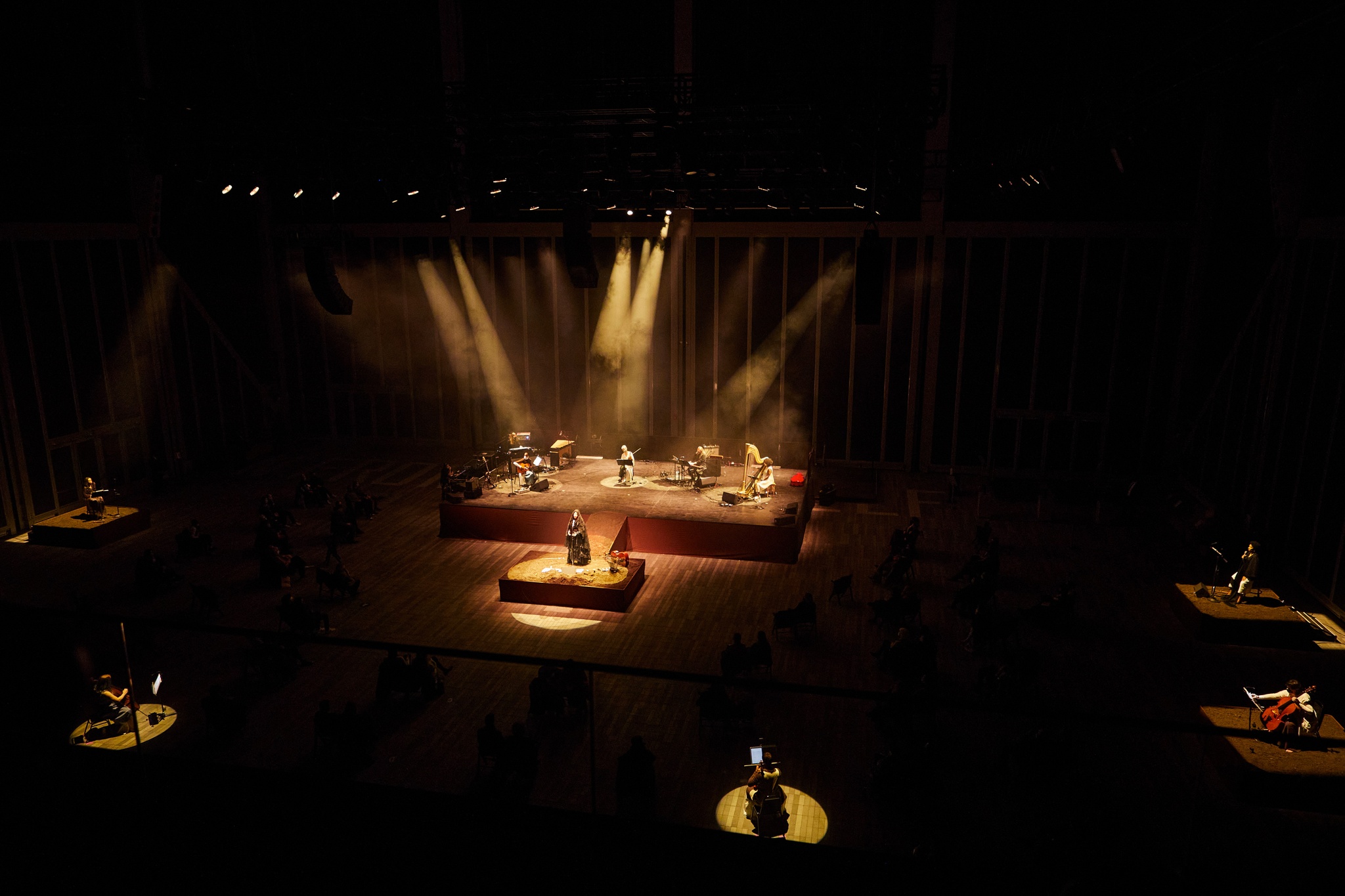 An aerial view of a spotlight stage in a darkened performance space with smaller satellite stages also illuminated around it. 