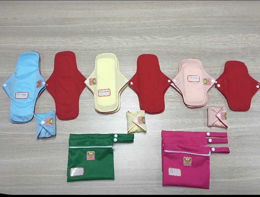 A color photograph shows menstrual pads and other menstrual products in blue, yellow, red, pink, and green.