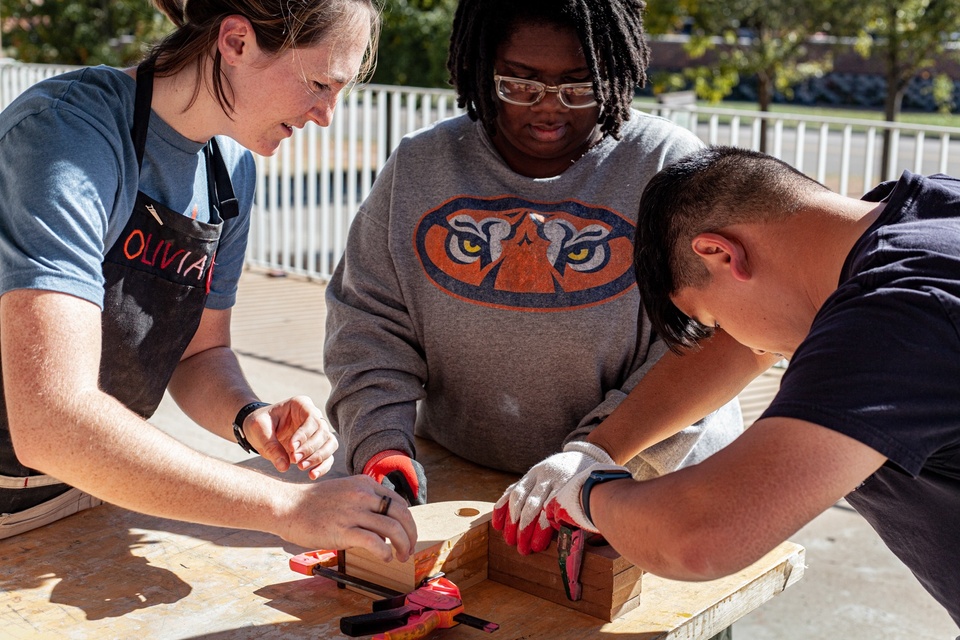 Three students working together to compress multiple slabs of wood with adhesive and clamps