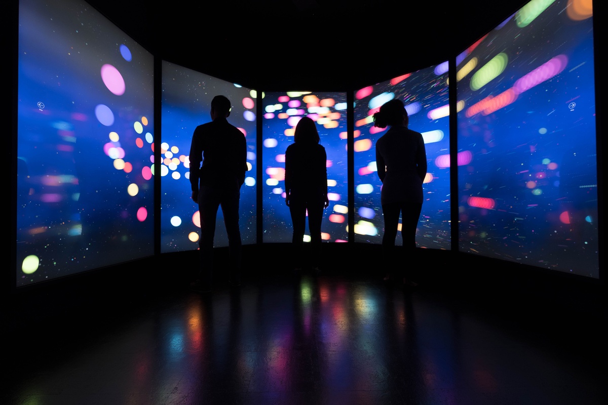Three silhouetted people standing before a large screen curved around the interior of the installation, which displays colorful and dynamic graphics