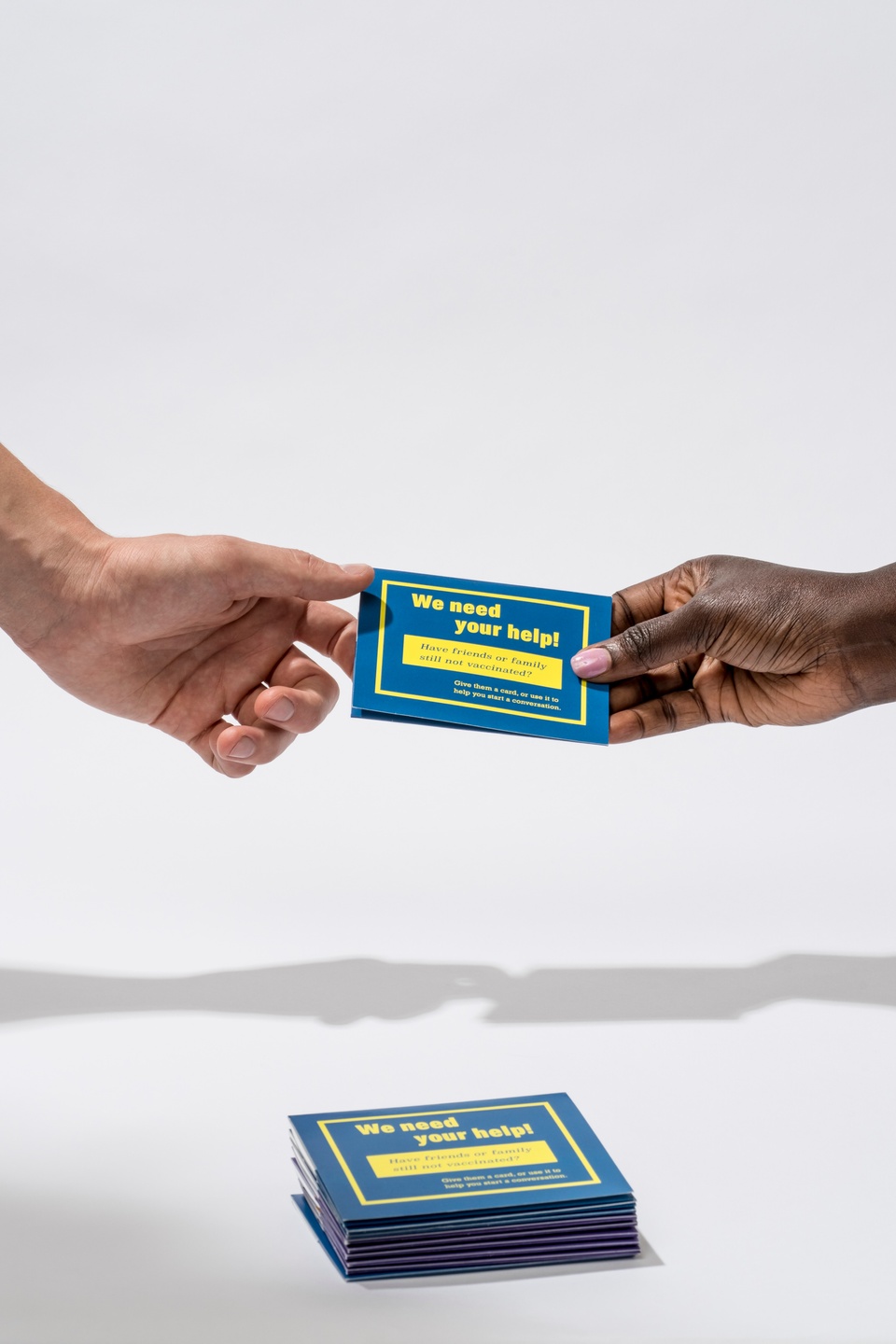 Cropped close, a woman hands a blue and yellow card holder to a man. A stack of extra holders is in front of them.