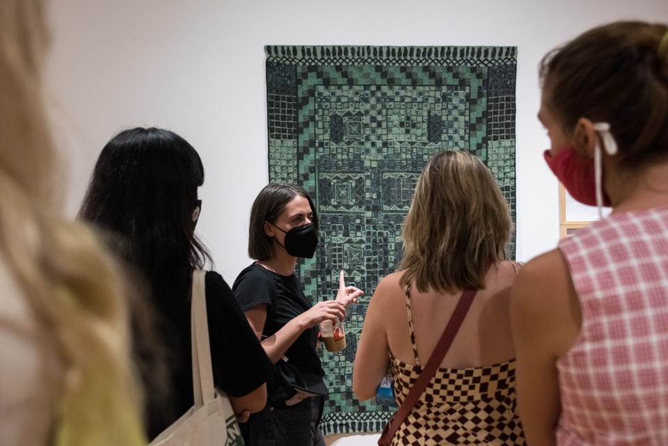 An artist standing in front of her fabric pattern artwork speaking to students