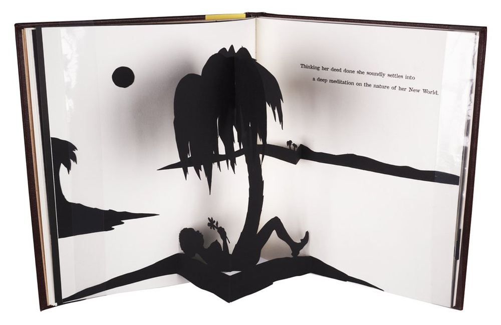 A book stands vertically, open to a white page spread with black pop-up structures depicting a silhouetted scene of a figure lying on their back and palm tree in center.
