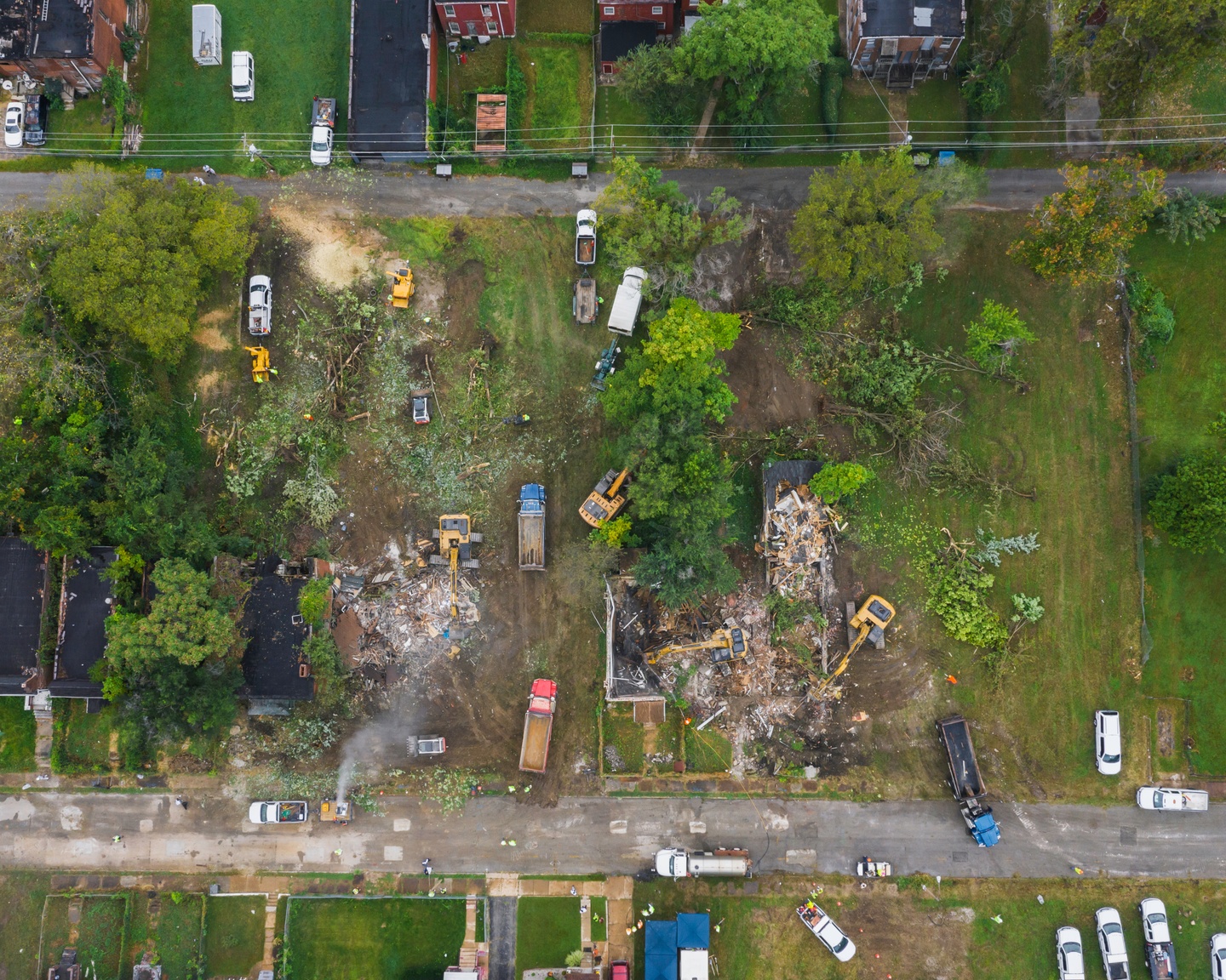Drone photo of a crew of bulldozers demolishing two brick houses on a neighborhood block.