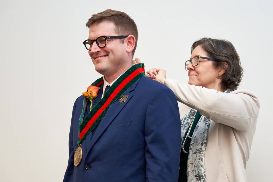 Woman places medallion around man's neck.