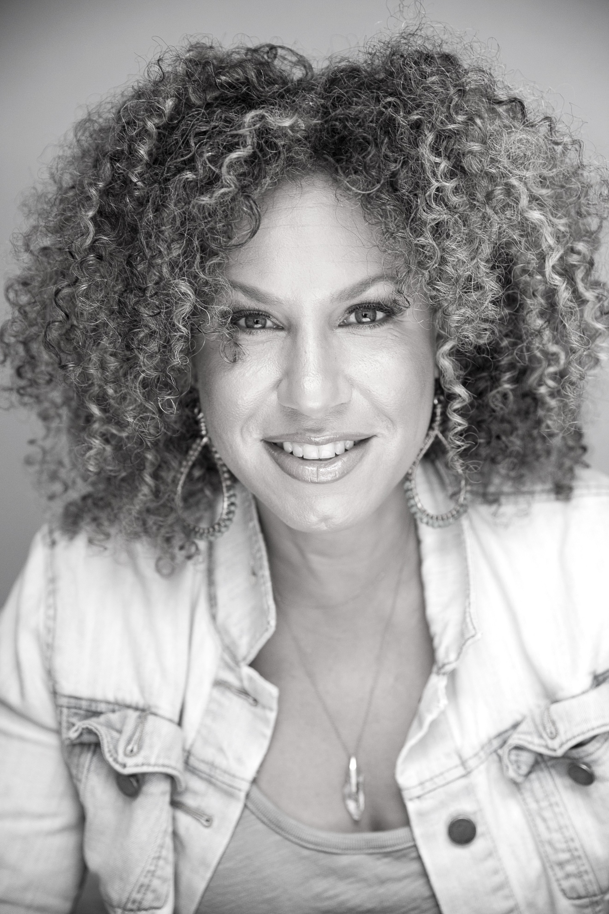 A black-and-white photo of Hopi Noel Morton. Morton smiles with raised eyebrows and curly hair parted in the middle framing her face. 