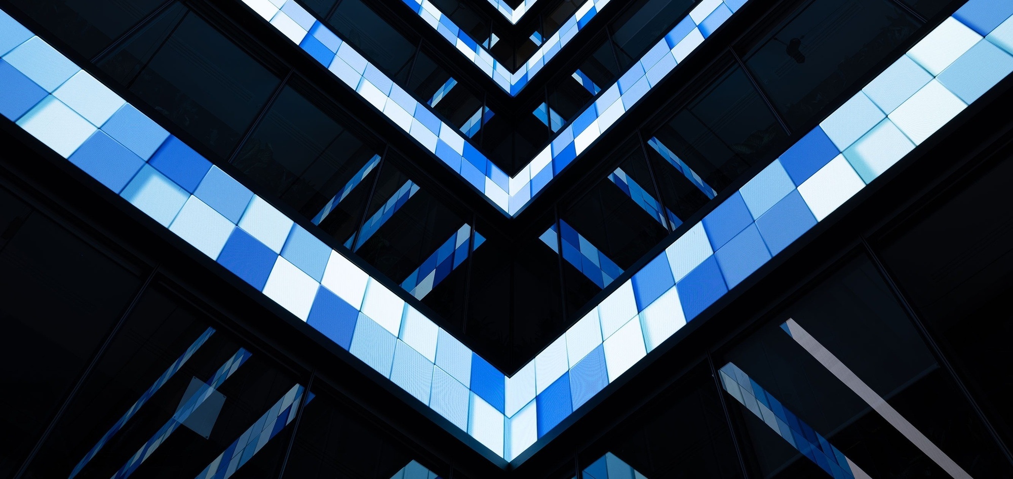 Four large-scale horizontal screens on the interior walls of the building atrium, displaying 3D blue and white square graphics