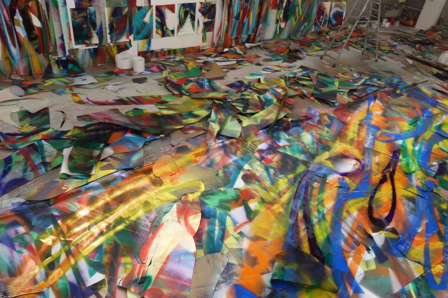 An artist's studio whose walls and floor are covered in sweeping, colorful brushstrokes and fragments of paintings