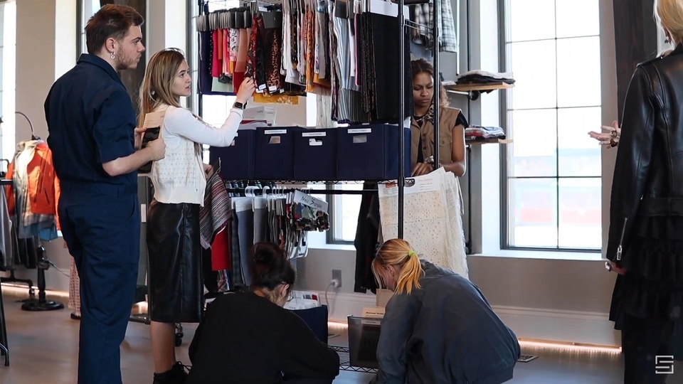 Students examine fabric samples on a rack