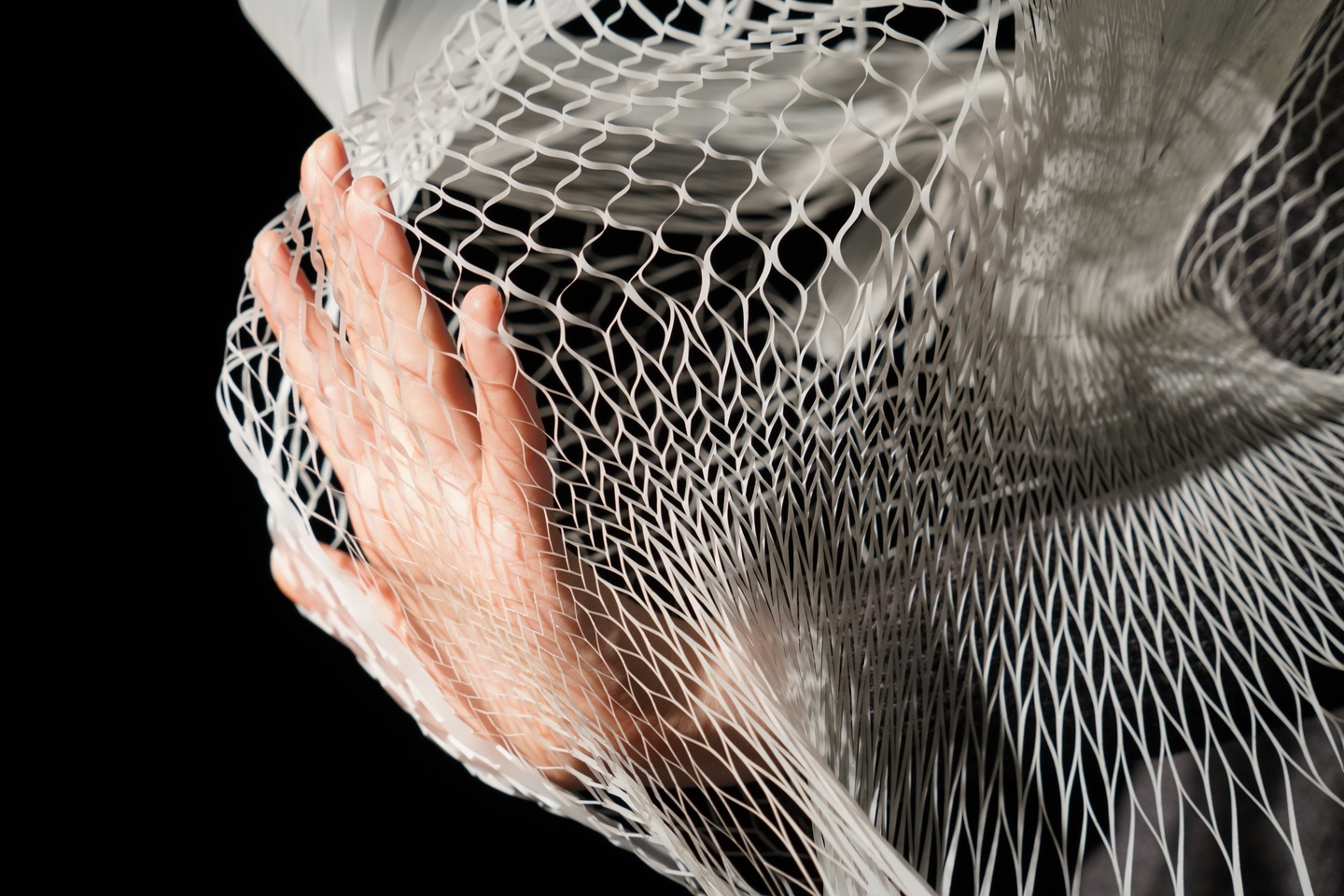 A hand presses against a white 3D printed mesh and expands it outward.