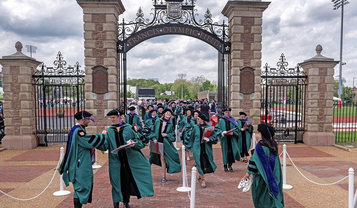 Throngs of graduates in caps and gowns walk through an archway for Francis Olympic Field.grads-Francis-Field-1200x700.jpg