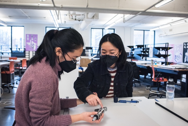 Two people at a drafting table look at a metal tool together.