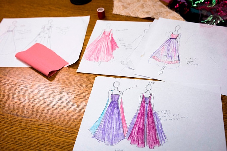Several fashion design sketches of dresses, as well as a fabric swatch, lying on a table.