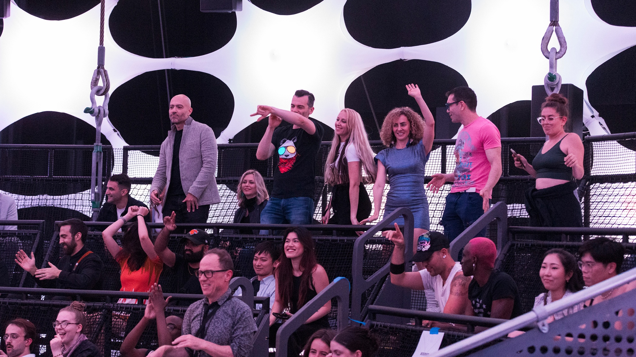 Visitors to Sonic Sphere stand and dance with their hands in the air. Behind them, the fabric of the sphere glows with a white light.