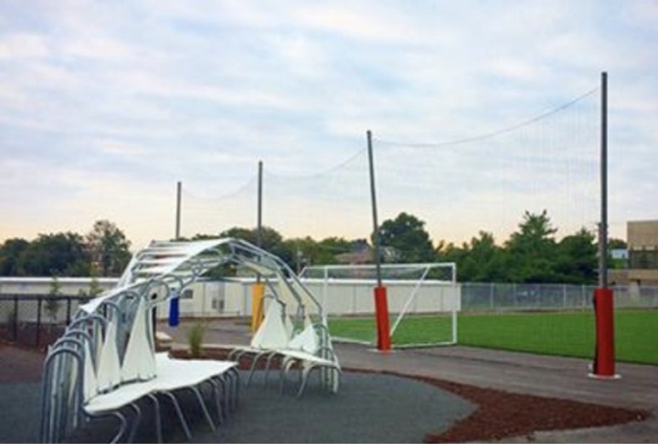 Shade structure made of geometric white forms sits in front of a soccer field.