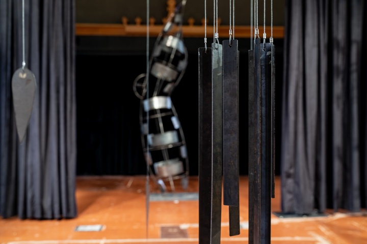 Close-up of long thin metal plates hung from cables in a cluster, similar to a windchime.