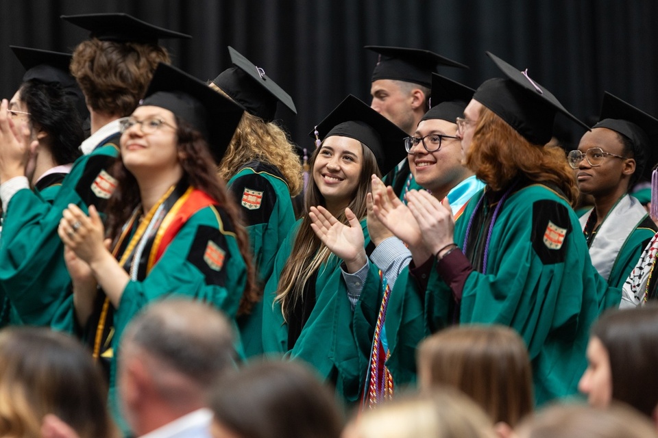 Group of WashU grads in green robes stands and applauds.