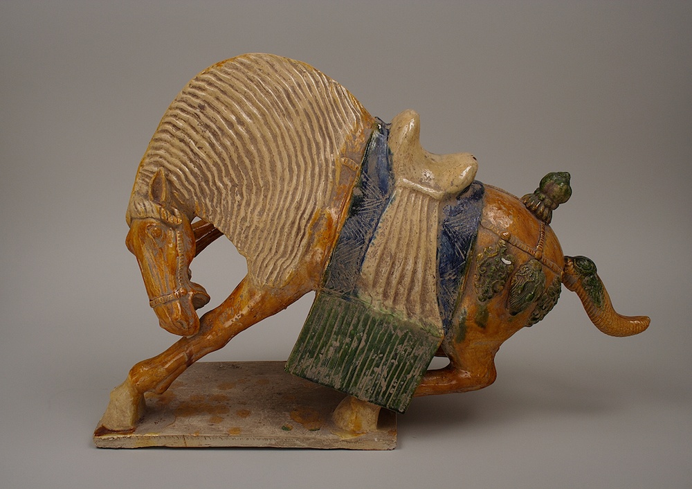 Ceramic statue of a horse reeling back with a blue, green, and yellow saddle.
