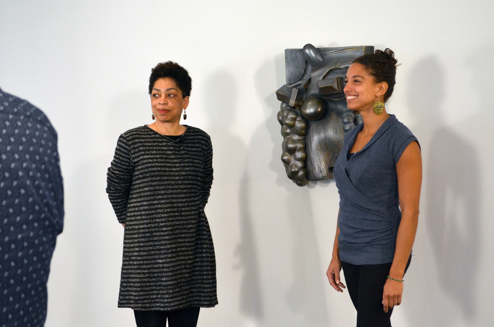 Syd Carpenter stands to the left of her sculpture, mounted on the wall behind Leah penniman