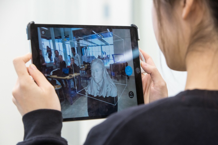 Person holds up an iPad with a piece of 3D scanning software running while they scan another person's head.