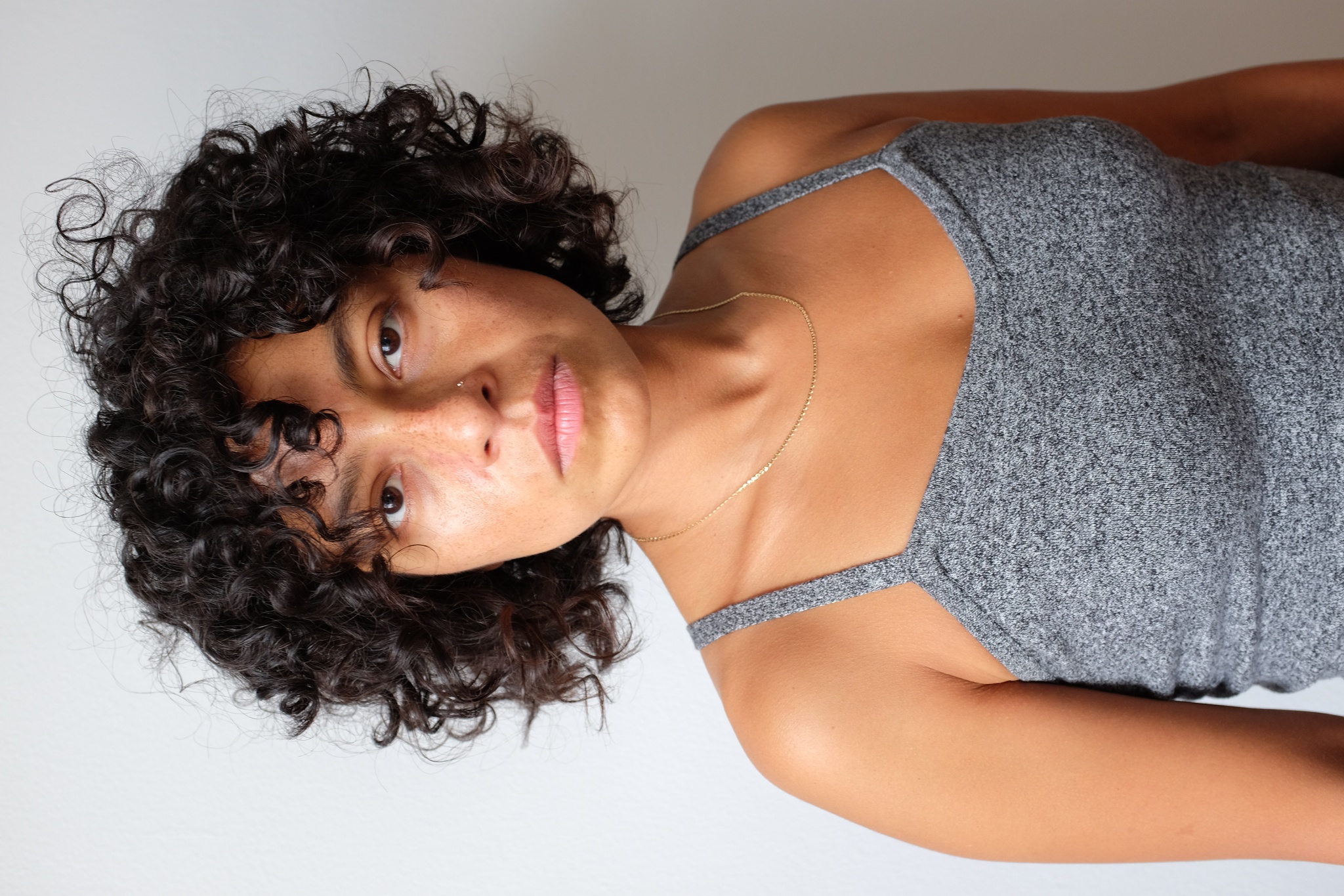A portrait of the artist Mariana Valencia wearing a gray tank top and with dark curly hair