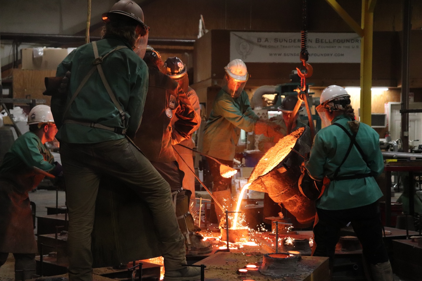 Students in PPE look on as red hot melted steel is poured into a mold