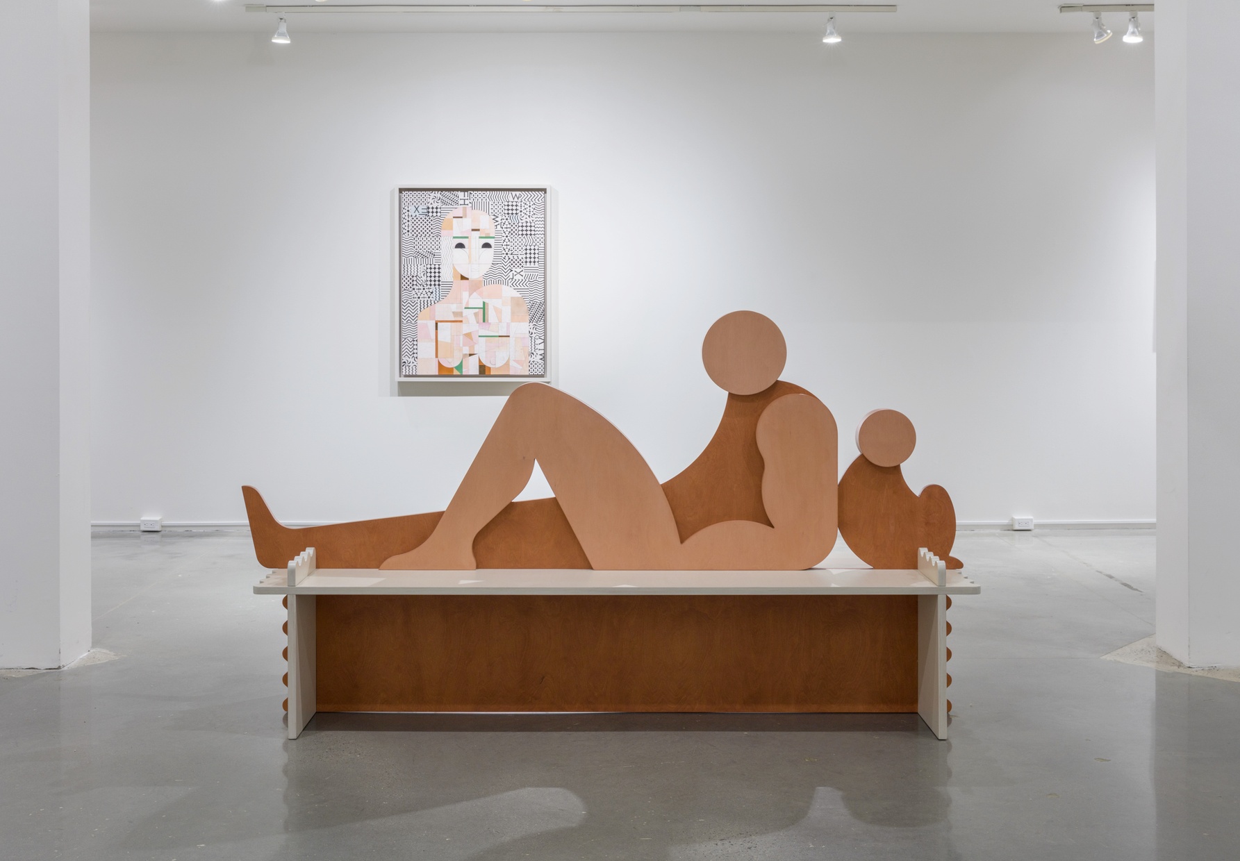 A sculpture of a large, brown, abstract figure reclining with one leg outstretched and one leg bent leaning against a small, crouched, abstract figure.