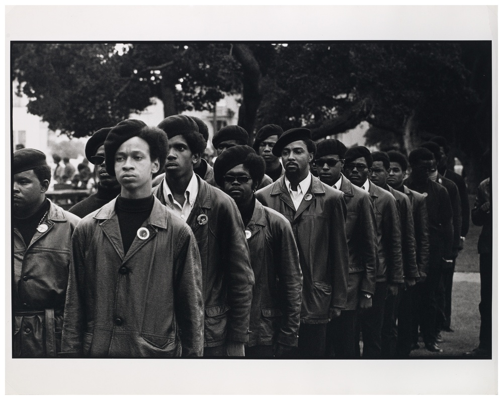 Black and white photograph of Black men wearing suits and beret hats lined up as if they are in marching formation.