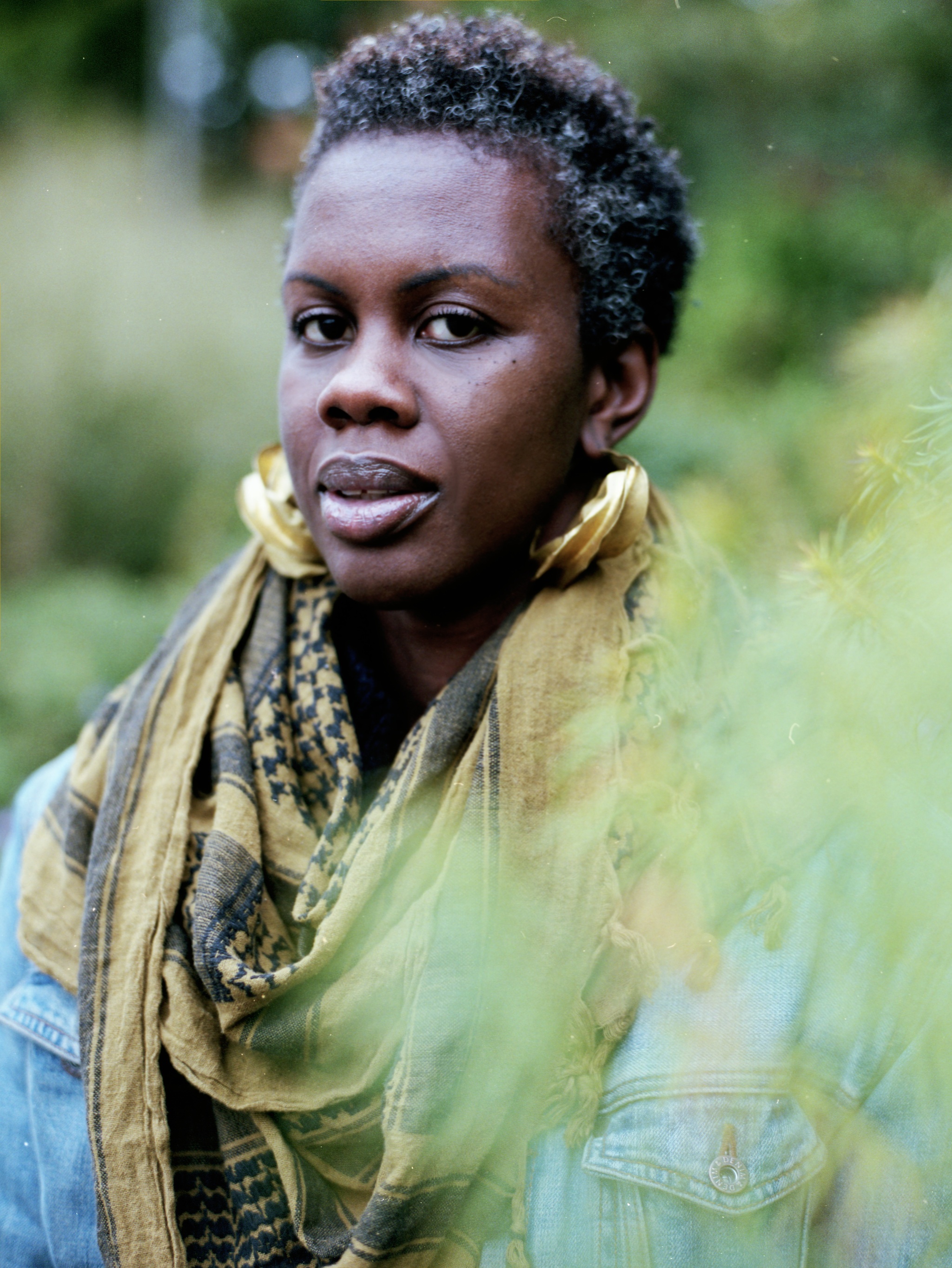 A portrait of Charlotte Brathwaite seen in three quarters view surrounded by trees and green branches
