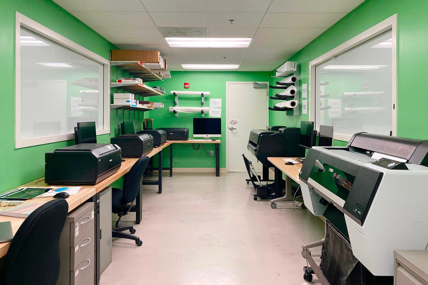 Room with bright green walls and long tables on each side with several printers sitting on top.