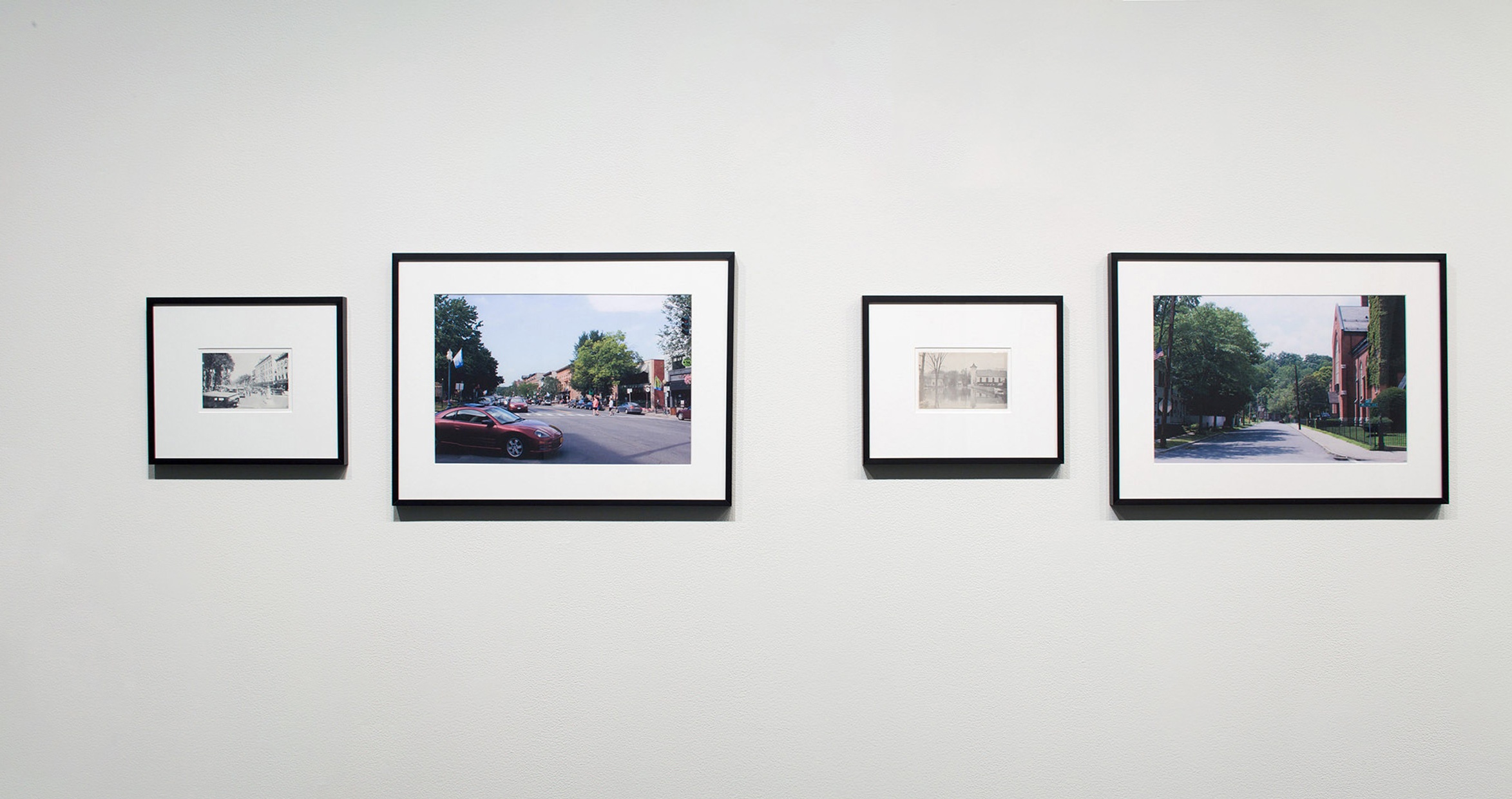 Four framed photographs, two black and white and two colored, of village scenes hang on a white wall.