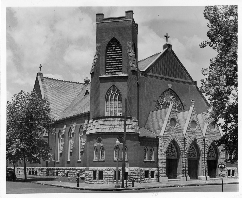 Black-and-white photo of a large church on the corner of a street, with trees to the sides.