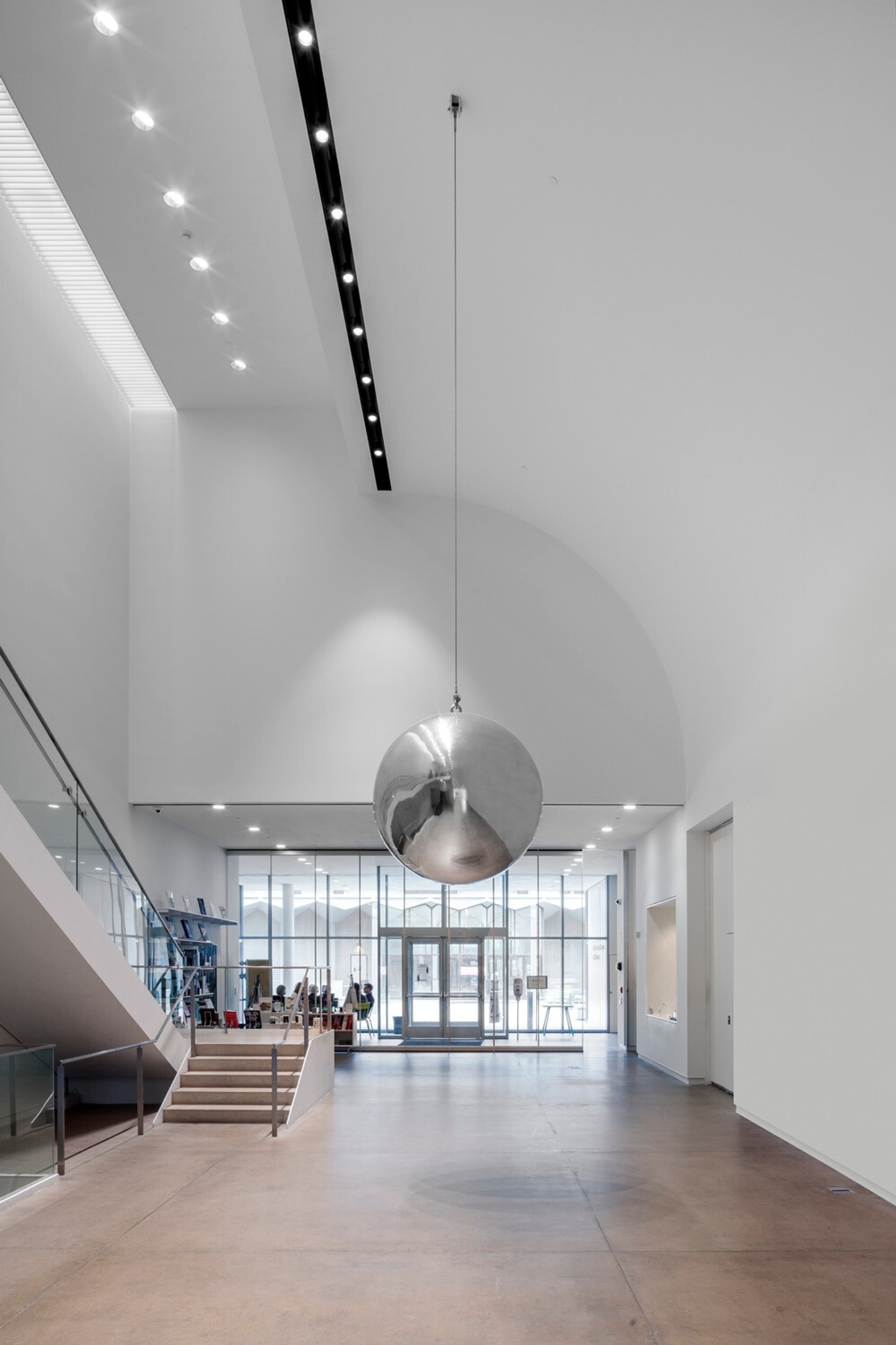 Installation view of Olafur Eliasson’s "Your Imploded View" in the atrium of the Kemper Art Museum. A large polished aluminum sphere hangs in the center of the open atrium, its reflective surface distorting the surrounding architecture.