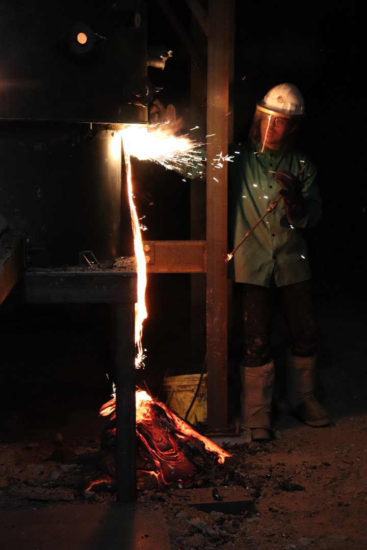 A person in PPE in a darkened area looks on as sparks fly.