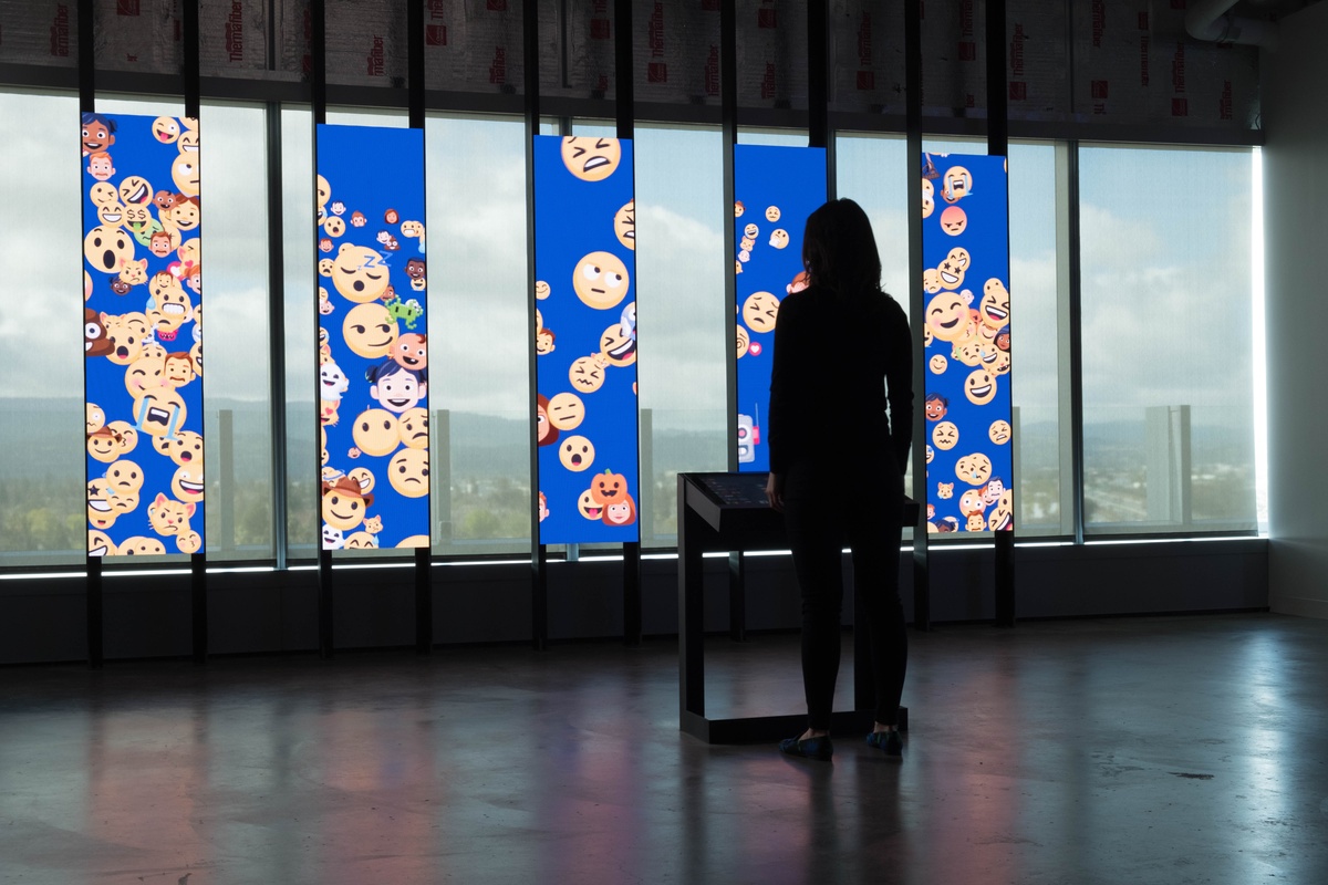A silhouetted person standing in front of five vertical panels that display a stream of emojis