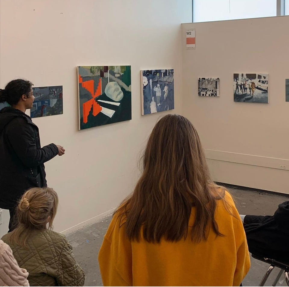 A student presents his paintings on display on a white wall in front of the class