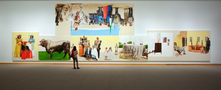 Museum installation of several brightly painted canvases. Five are lined up in a row on the bottom; one hangs above them, hung upside down.