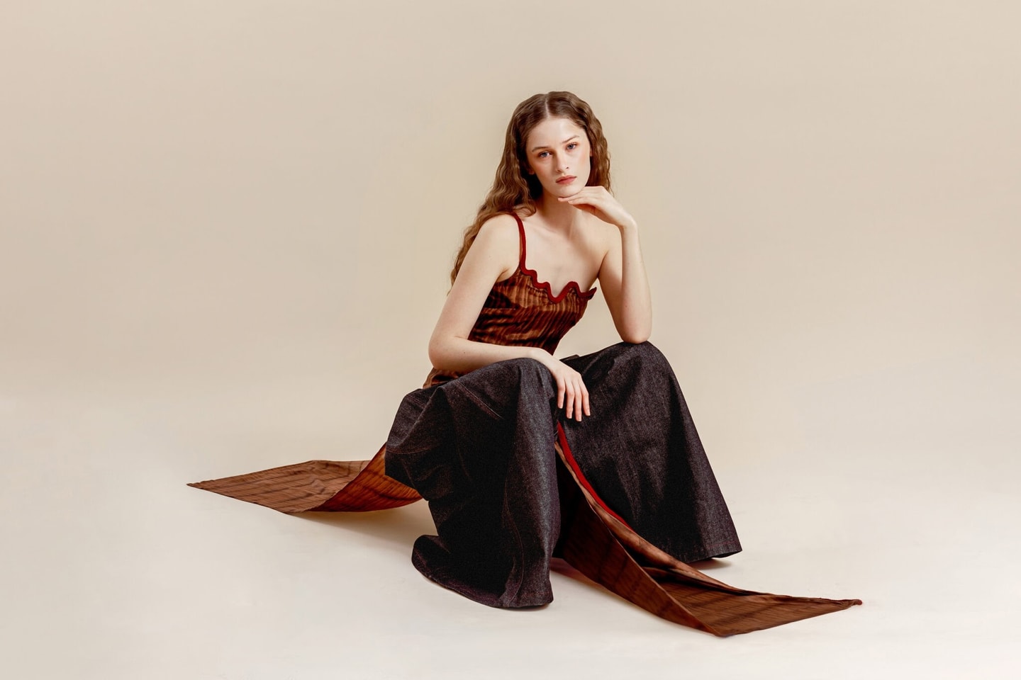 model is crouched down wearing a one strap red top with wide black pants and red fabric flowing front and back