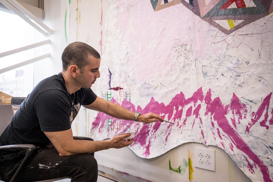 Student paints a pink mountainscape on a white, unevenly shaped canvas.