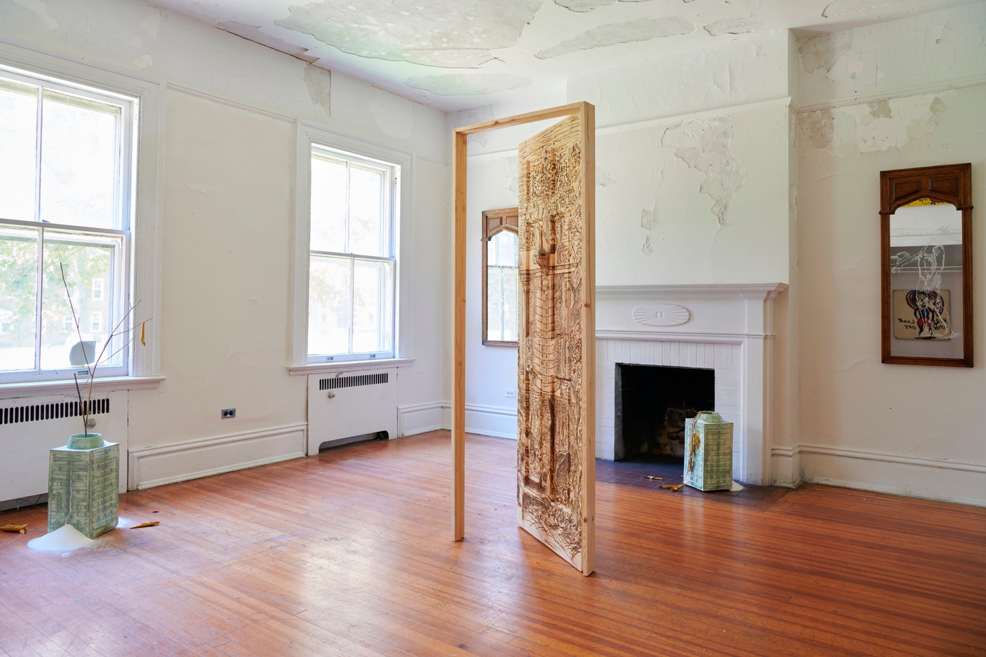 Artwork installation in the room of a house, featuring a door frame made of burnt pine; the door itself is ajar, with intricate black etchings.