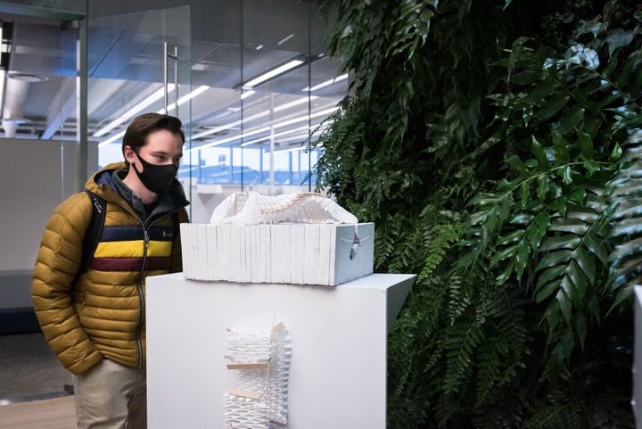 Person looks at a white model with two components: a folded paper model twisted into a curve, sitting on top of a stack of white concrete plates.