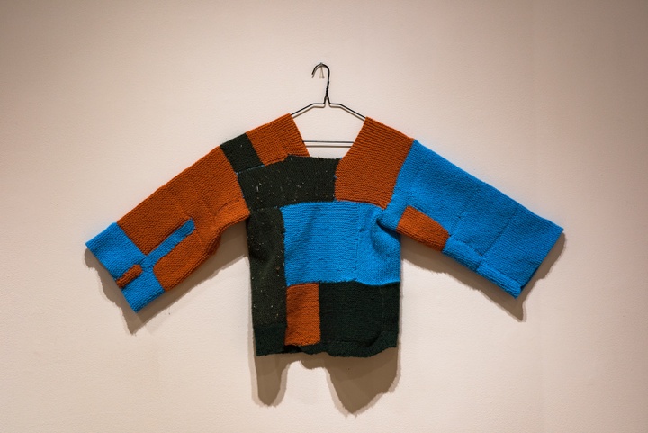 Knit sweater with a square neck and blocky rectangular sleeves made from irregular blocks of bright blue, black, and rust-colored yarn.