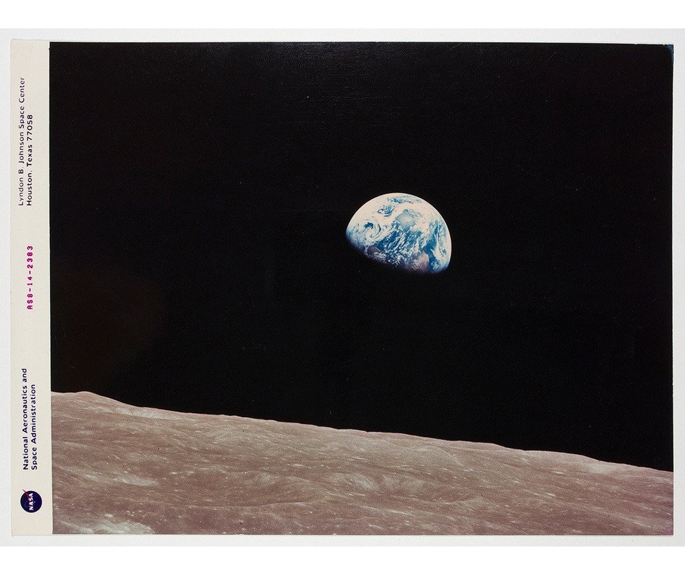 Photograph taken from the moon, where the moon surface is in the foreground and the earth is rising in the distance.