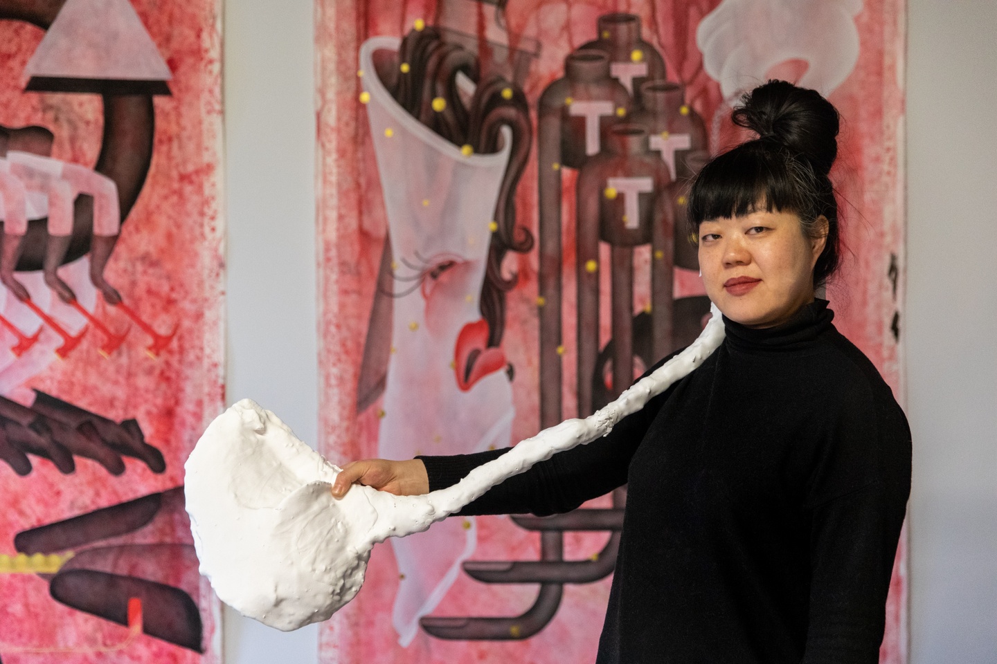 woman holding a plaster sculpture with bright pink art hanging behind her