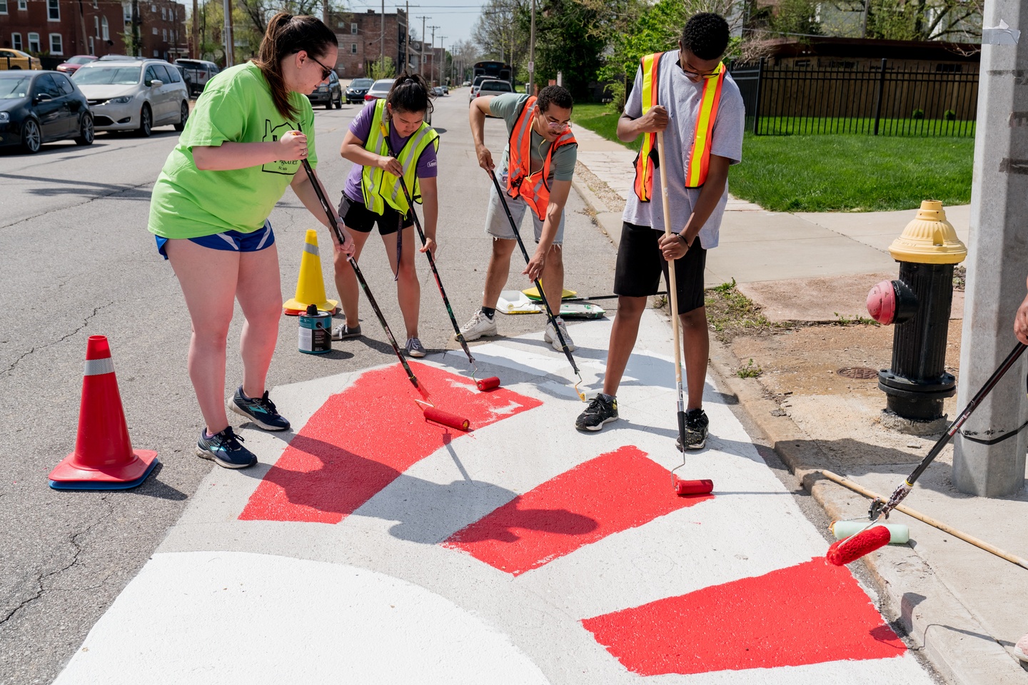 Four individuals are painting a mural on an asphalt street.