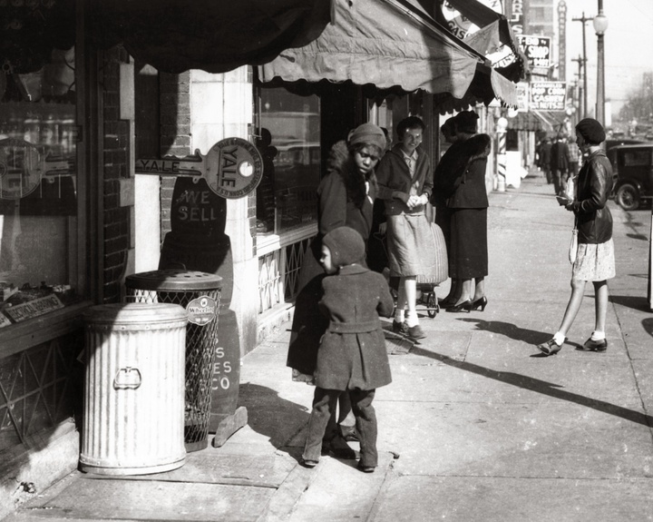 Shoppers standing on the sidewalk in front of businesses.