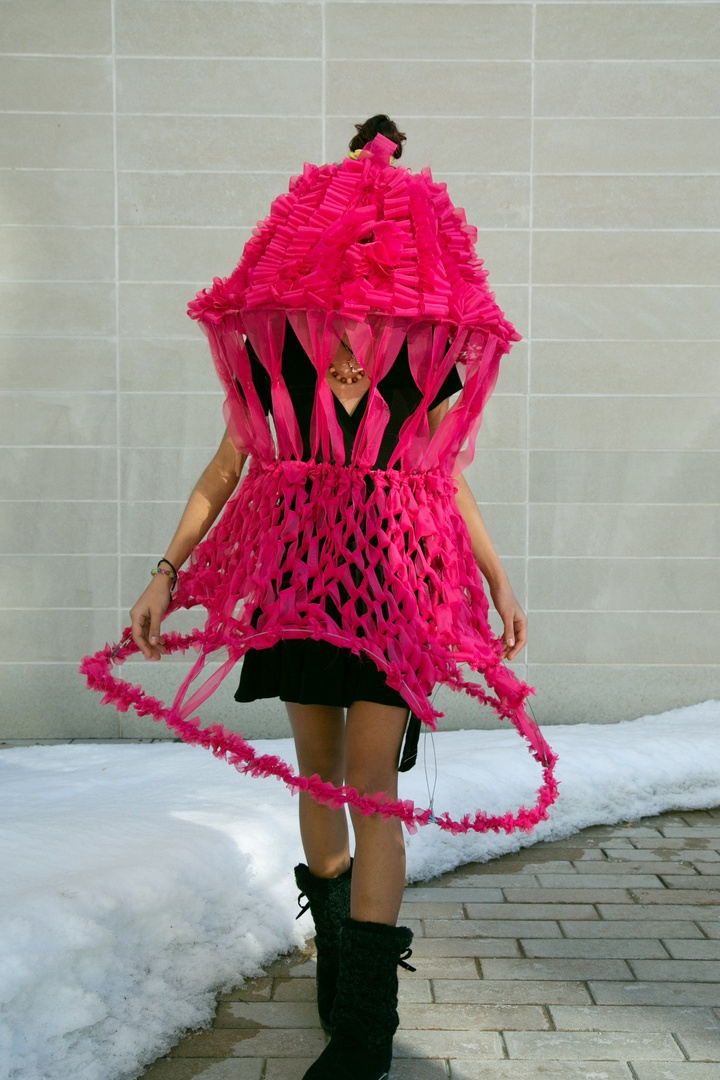 Person wearing a large, fuschia hat structure that envelopes the person.