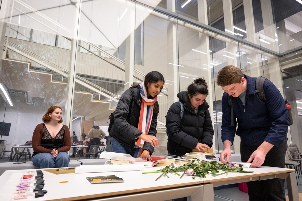 Three students gather around a table with cut flowers and books for pressing them.