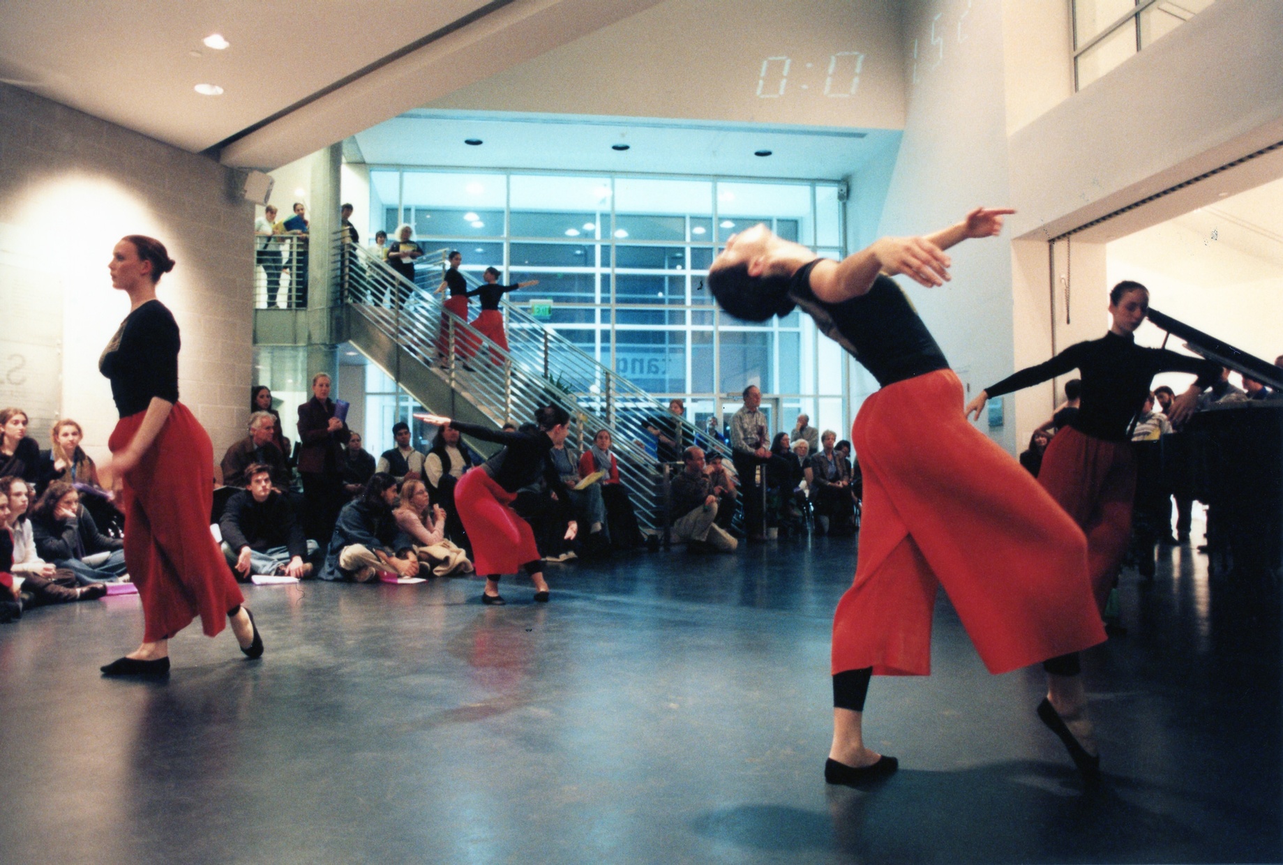 A group of dancers perform in an open space with a crowd of people sitting on the floor around them.