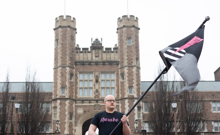 Alex Rosborough Davis standing in front of building holding a flag